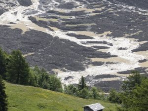 epa12148726 Water from the Lonza river flows over the mud and stone, after the formation of a lake on the last houses of the village of Blatten, Switzerland, 01 June 2025. A large part of the Blatten village, located in the Loetschental Valley in the canton of Valais, was buried under masses of ice, mud, and rock on 28 May after several million cubic meters of rock fell from the Kleines Nesthorn mountain above the village, resulting in the collapse of the Birch Glacier. EPA/CYRIL ZINGARO