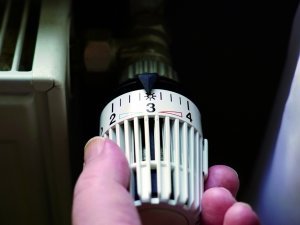 hand turning down thermostat on radiator to save energy due to heating cost price hike