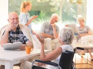 Elderly man talking with disabled woman while sitting together at table in common room