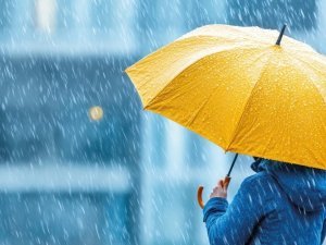 Una persona se encuentra de pie en medio de una intensa lluvia en la ciudad, sosteniendo un paraguas amarillo. La atmósfera es tranquila y melancólica, mientras las gotas caen alrededor.