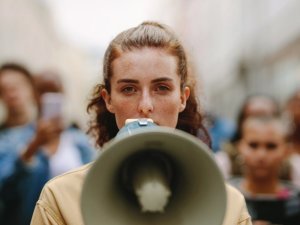 Female activist protesting with megaphone during a strike with group of demonstrator in background. Woman protesting in the city.