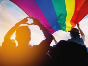Pride community at a parade with hands raised and the LGBT flag.
