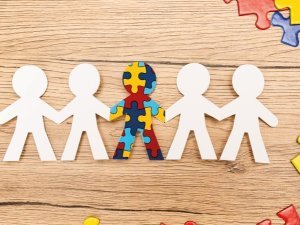 Top view of special kid with autism among another and pieces of multicolored puzzle on wooden background