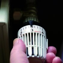 hand turning down thermostat on radiator to save energy due to heating cost price hike