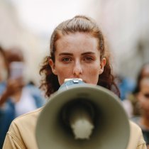 Female activist protesting with megaphone during a strike with group of demonstrator in background. Woman protesting in the city.
