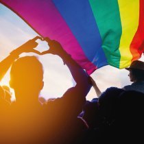 Pride community at a parade with hands raised and the LGBT flag.